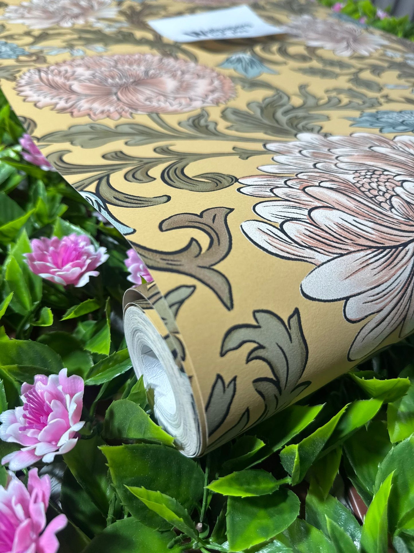 Mustard Floral Wallpaper roll close up amongst pink and green garden flowers